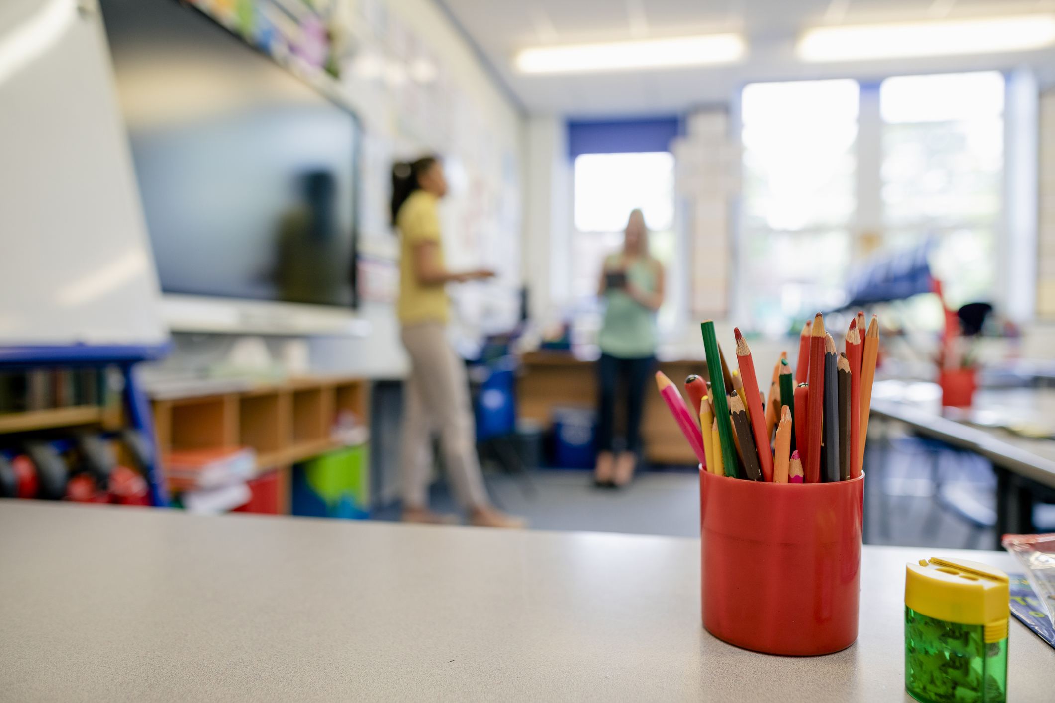 A pencil organizer is standing on a desk in a classroom.